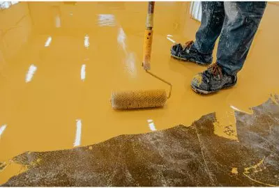 a person applying epoxy coating to a concrete floor with a paint roller