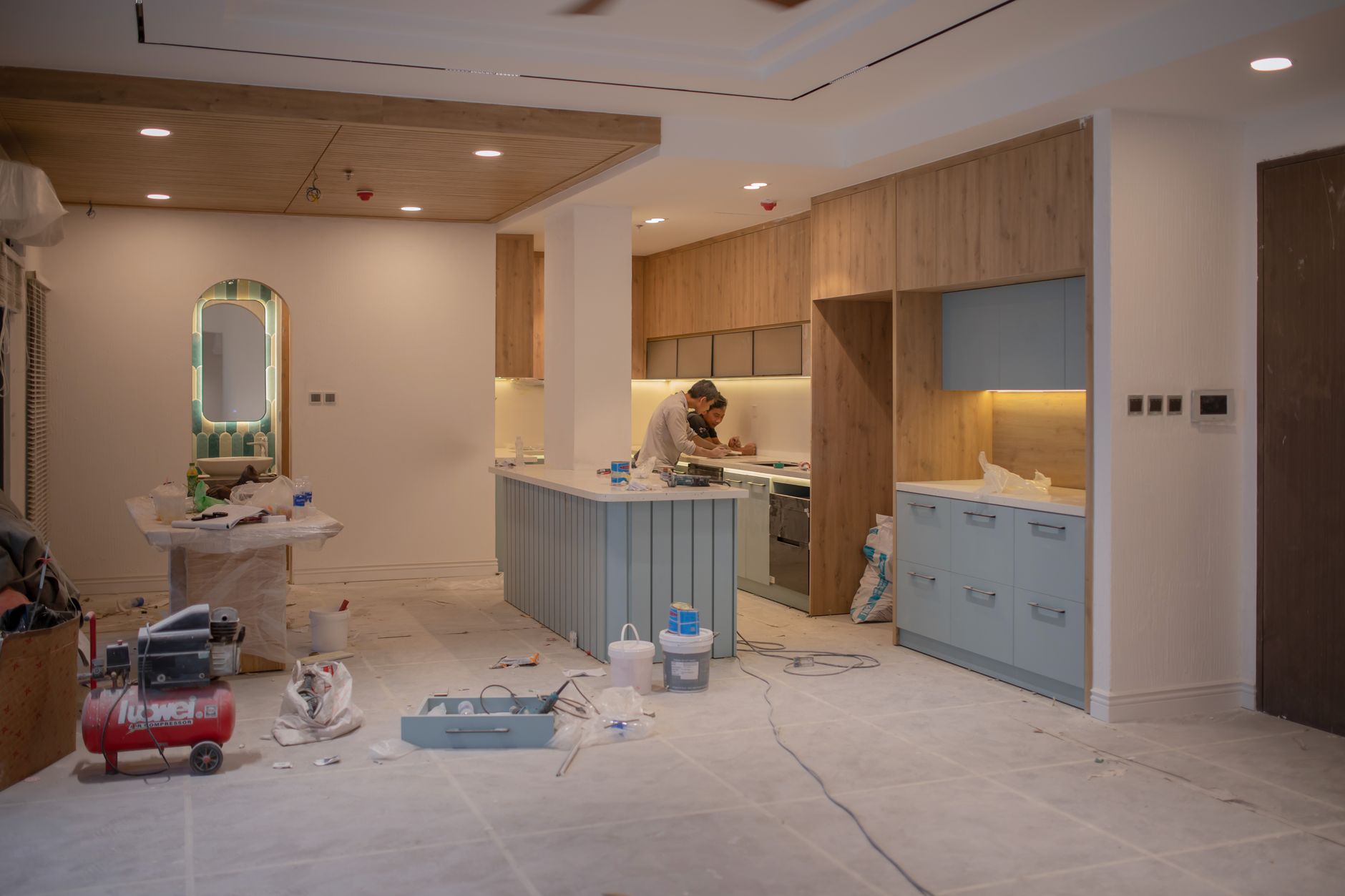 A kitchen mid-renovation with a worker prepping cabinets, tools, and materials laid out for a cabinet painting project in Port St Lucie